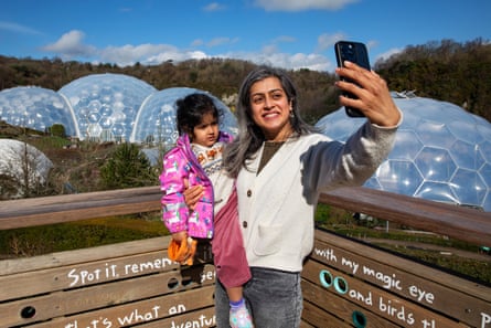A woman holding a young child in one arm takes a selfie in front of the biomes