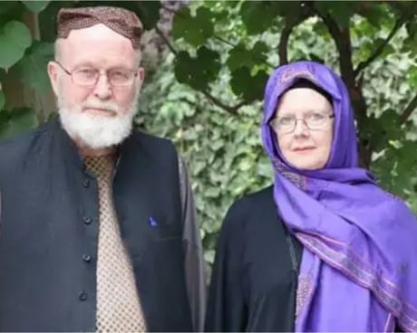 An elderly couple dressed in Afghan clothes with the woman wearing a purple scarf over her hair