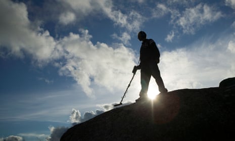 Man with metal detector silhouetted against cloudy blue sky.