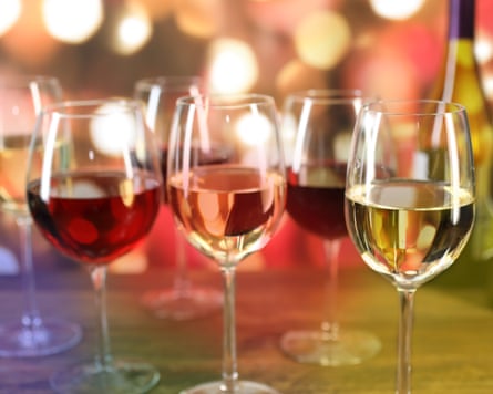 Various Christmas, New Year’s Eve holiday wines in wine glasses with bottles and lights in background.