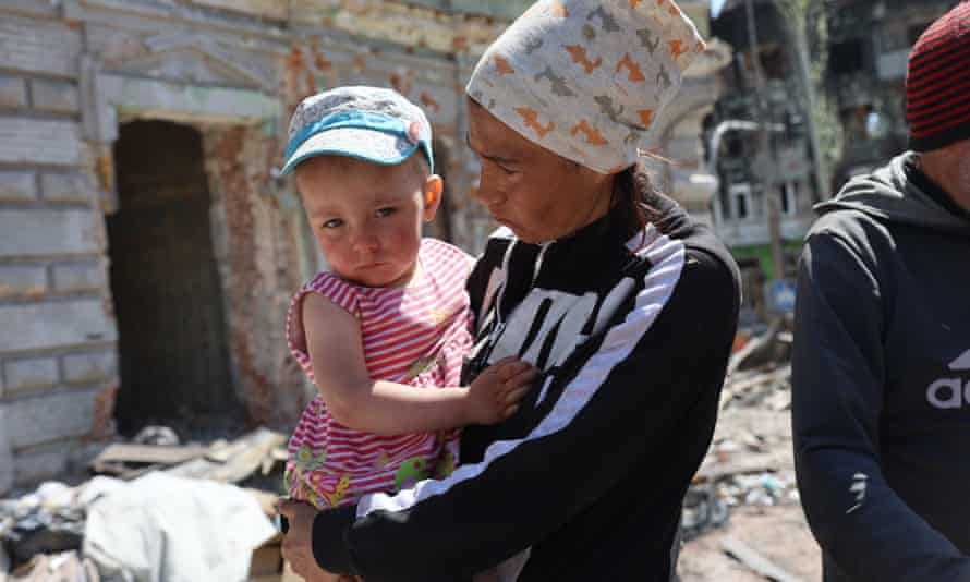 A woman carrying her baby is seen in front of damaged residential building in Ukraine’s Mariupol.