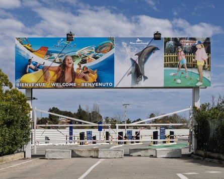 A sign advertising a marine park over a road that has been blocked by concrete blocks