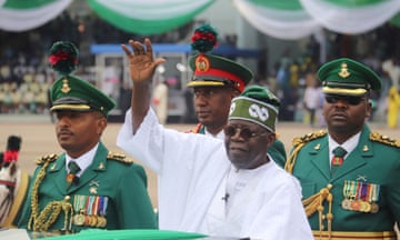 Bola Ahmed Tinubu raises his hand flanked by military officials during an honour guard