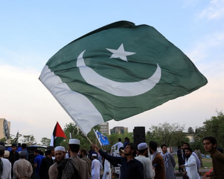 the large flag, which is dark green with a white crescent and star, is flown against a pale blue sky
