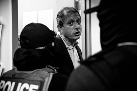 A man in a suit speaks to masked agents