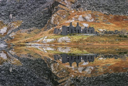 Abandoned slate mine buildings of Cwmorthin and its mountainous background reflected in the waters of a lake.