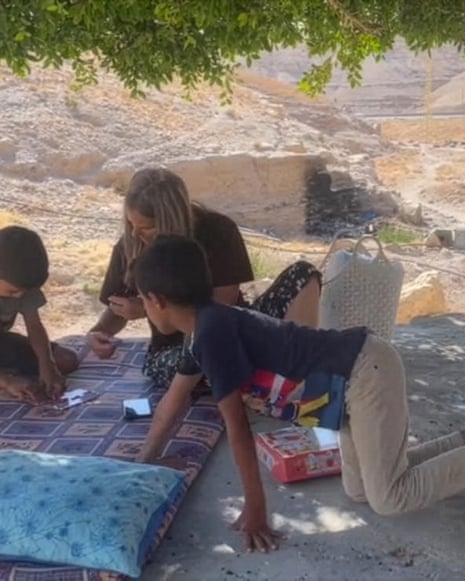 Two boys and a woman sit on a mattress outdoors, playing cards near Jericho