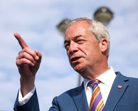 Nigel Farage in a navy suit and colourful striped tie gestures with his finger raised while speaking outdoors