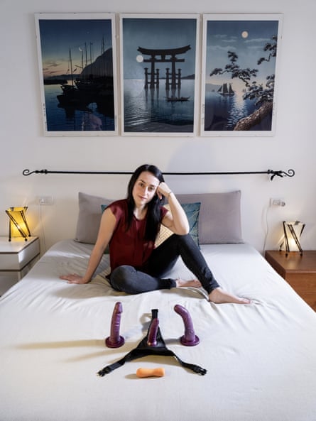 Portrait of Serena sitting on a bed with her sex toys laid out in front of her