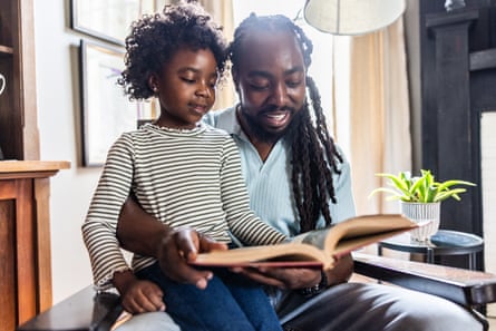 Father and young daughter reading a book in home library