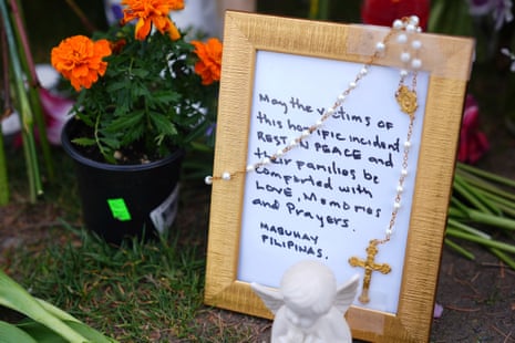 a handwritten framed note says 'may the victims of this horrific incident rest in peace and their families be comforted with love, memories and prayers' at a memorial site