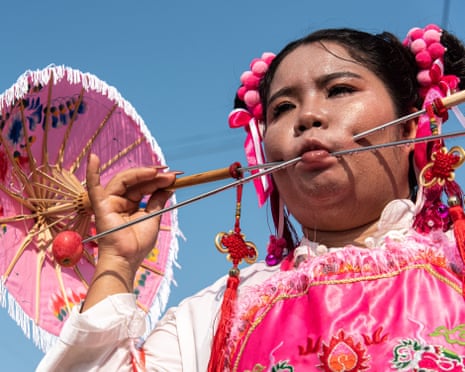A devotee with an umbrella-decorated skewer pierces her cheek