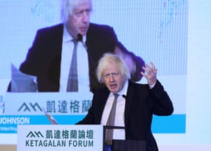 Boris Johnson gesticulates as he speaks from a lectern in front of a video projection of him