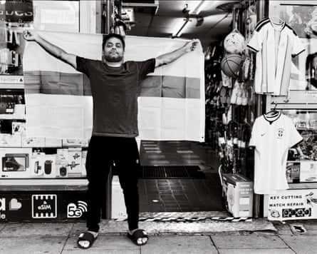 A man stands outside a shop holding an England flag up behind him