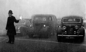 Policeman on point duty in 1952 using flares to guide the traffic during a London peasouper.