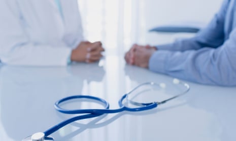 Stethoscope on white desk in doctors office, female doctor and patient sitting in background