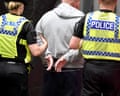Two police officers escort a handcuffed man in a grey hoodie