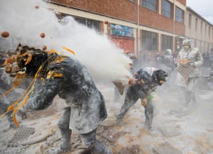 Flour and eggs burst over two crouching revellers, as another flour-covered man carries eggs towards the battle
