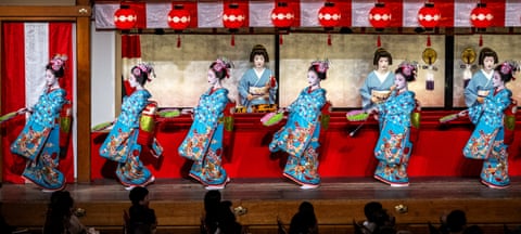 Women wearing blue geisha costumes perform on stage, walking in a row