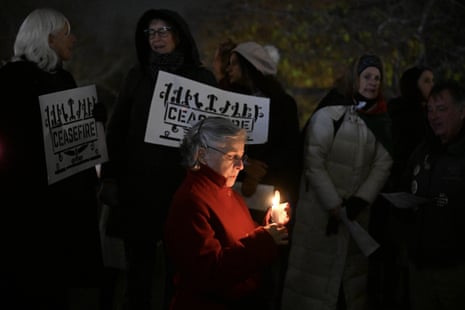 A woman with a candle and people holding signs saying “ceasefire” in the background