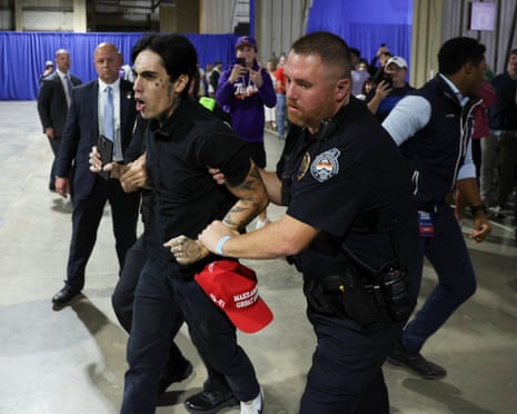 Security removes a protester, dropping a red cap, from a Trump rally