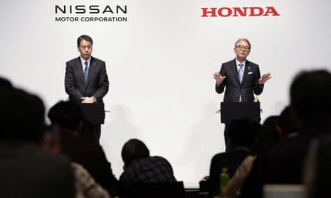 two men in suits stand on stage under either the Nissan or Honda logos