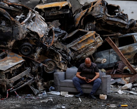 A man who says he survived an Israeli strike last week sits beside piled damaged cars at the site at Corniche al-Mazraa in Beirut, Lebanon