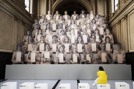 Inside a church with a black and white cutouts of people holding cards arranged in stepped rows