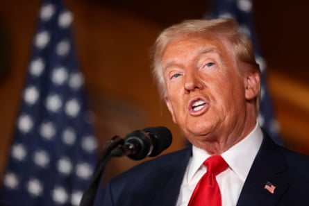 Donal Trump in front of microphone with US flag behind him.