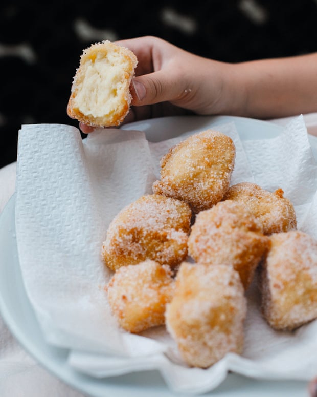 Un piatto di crema fritta.  Le metà della crema pasticcera fritta sono ricoperte di zucchero e appoggiate su un tovagliolo di carta sul piatto.  Una mano che tiene quello mezzo mangiato