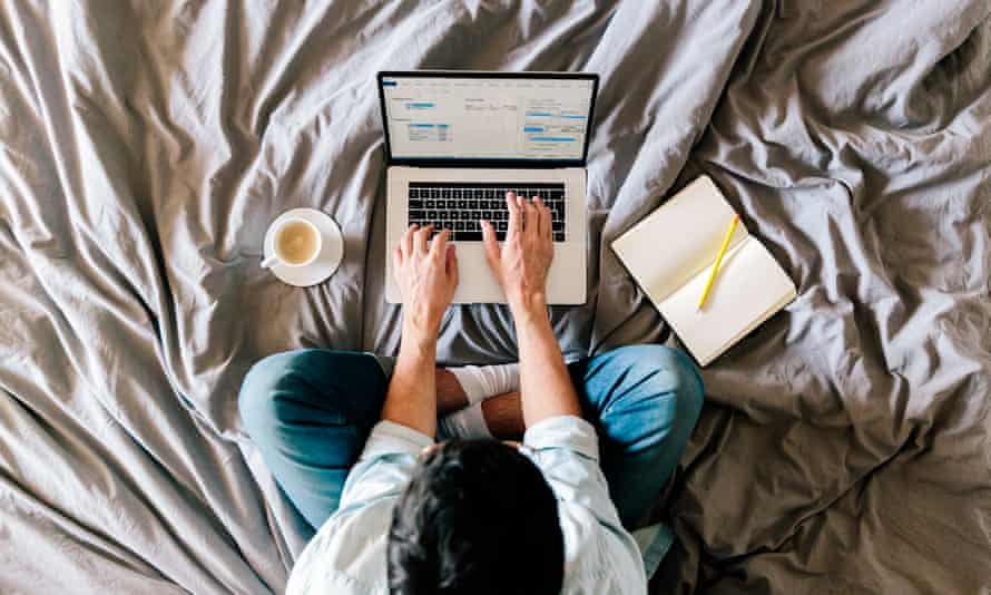 A man sitting on his bed working on a laptop.