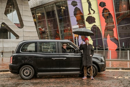 Ben holds an umbrella while standing next to a black cab with John Consterdine at the wheel outside the Lowry centre
