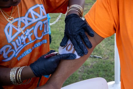 A person holding a template that says âÂÂ901â on someone arm before spray painting it to their body.