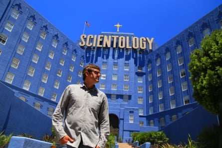 Louis Theroux outside a huge blue building with a massive gold sign reading “scientology”