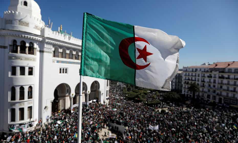 An Algerian flag flies over demonstrators protesting against President Abdelaziz Bouteflika in Algiers