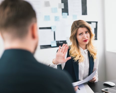 A young woman in business attire holds up her hand in a 'no' gesture to a man in a suit