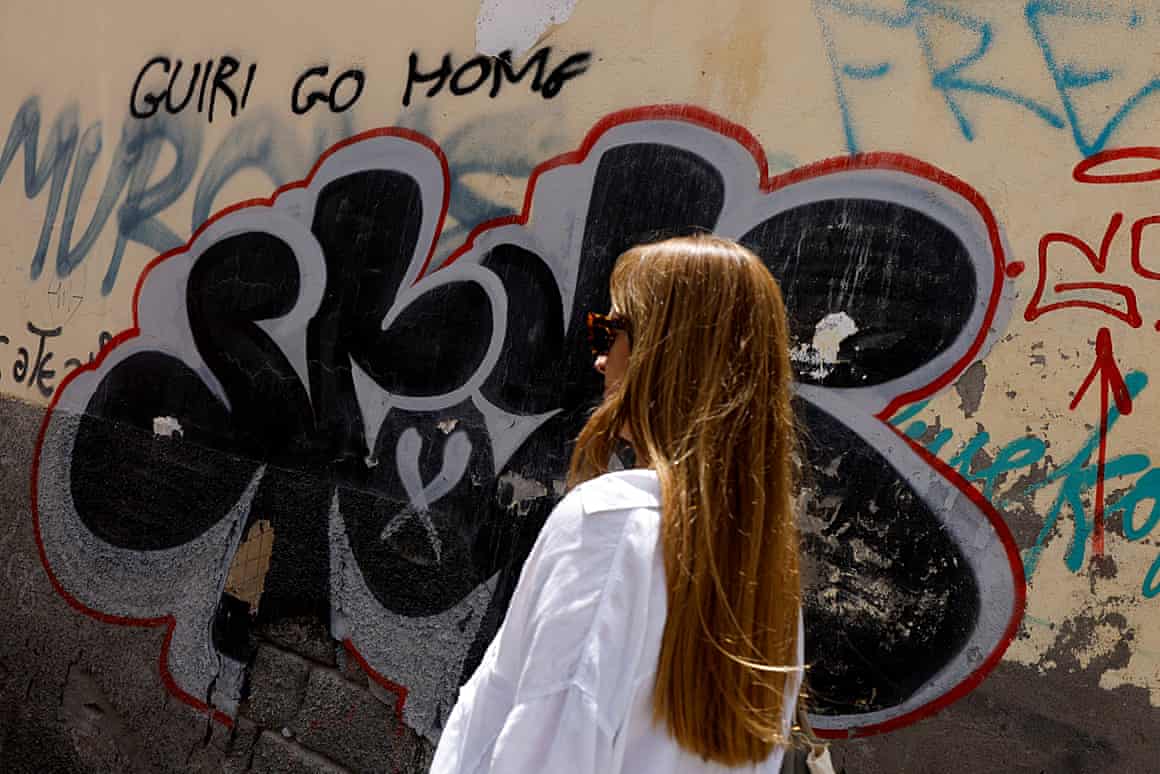 A woman walks past graffiti on the wall that says ‘tourist go home’