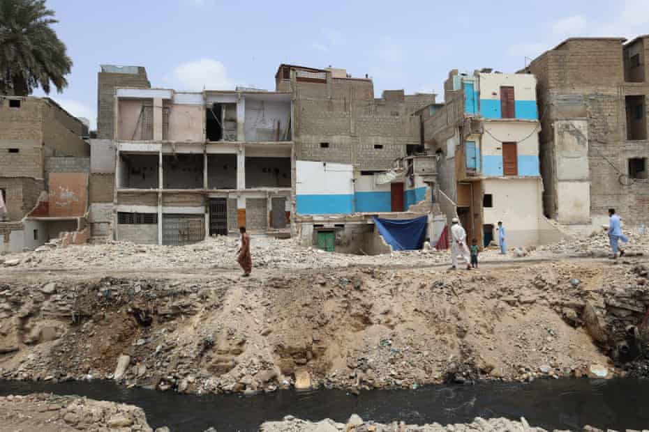 A man is walking on to rubble where there used to be houses in Gujjar Nullah; houses in the background are seen damaged