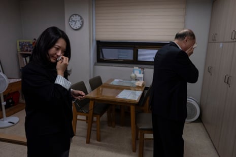 A woman and a man cry into tissues as they stand in a house together