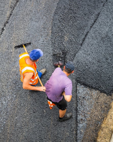 Two road workers spreading asphalt on a road, seen from directly above