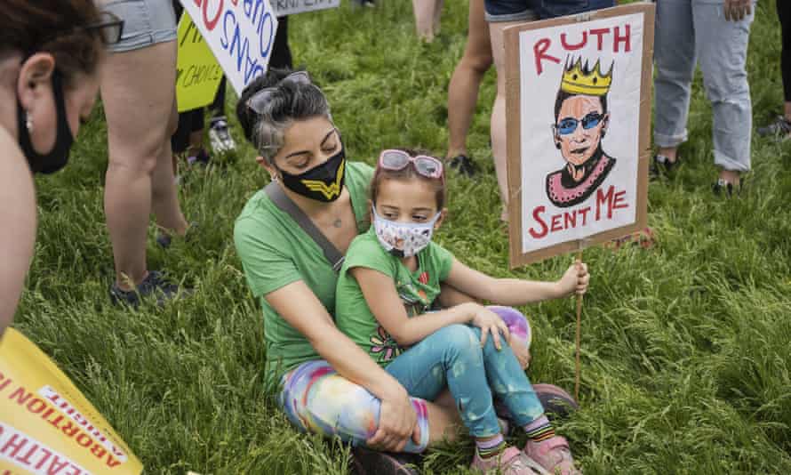 Protesters sit on the grass while holding a Ruth Bader Ginsburg during a protest Saturday morning, May 14, 2022
