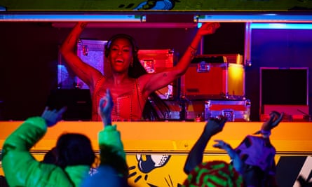 In a bus during a Glastonbury festival music sest, DJ Honey Dijon – with long hair, grinning and wearing a corset – waves her arms in front of people with their arms in the air