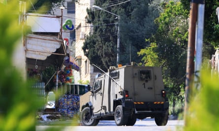 A grey-green armoured vehicle on a street in Nablus, seen framed by greenery in the sunlight