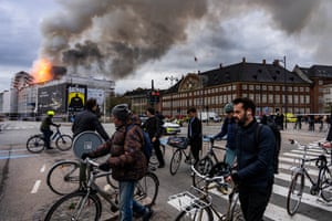 People ride bicycles as smoke rises from the Old Stock Exchange in Copenhagen