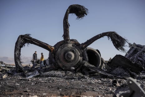 What appears to be the wreckage of a large engine turbine with people near against blue sky