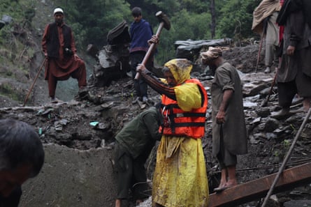 A person wearing a yellow poncho and orange life vest lifts a sledgehammer