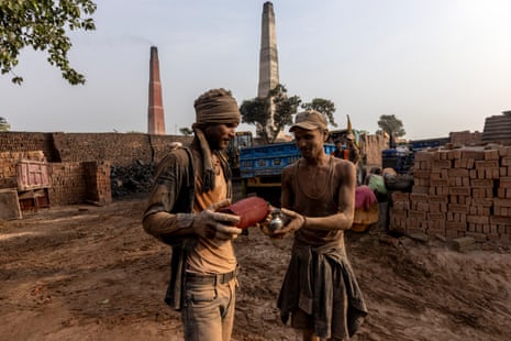Two men covered in dust stand together, one puring water from an insulated flask into a metal cup the other is holding.