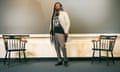 Black man with very long dreads, wearing black T-shirt, cream blazer, and gray khakis poses in front of long chalkboard between two chairs.