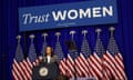 women speaks at podium in front of american flags and sign reading 'trust women'
