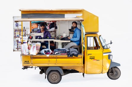 Tailors Bhola and Akash in a Piaggio van in Nashik, Maharashtra, India. It is a yellow van and the tailors sit in the back of it while working at a sewing machine